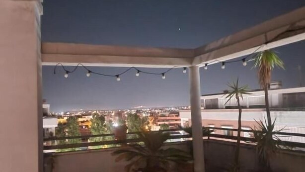Una terraza en la azotea con plantas en macetas, luces colgantes y vistas de la ciudad de noche.