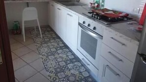 Una cocina con armarios blancos, estufa y piso de baldosas.