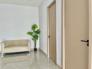 Ein Zimmer mit einem beigefarbenen Sofa, einem Topf mit Pflanze und einer Holztür.