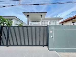 A gated residential area with a modern house, a metal gate, and a utility box. - Facai Star Villa C25 (Banglamung)