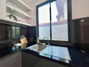 A modern kitchen with a black countertop, stainless steel sink, and a window with a view of a red-roofed building. - Facai Star Villa C25 (Banglamung)