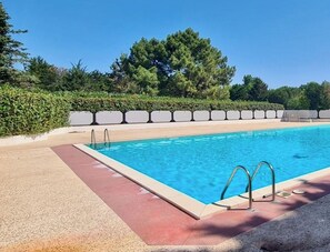 Ein rechteckiger Pool mit klarem, blauem Wasser, umgeben von einer Betonplattform und einem niedrigen Heckenstreifen.
