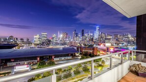 Stadsbeeld in de schemering met moderne gebouwen, een parkeerplaats en een balkon met uitzicht op de stad.