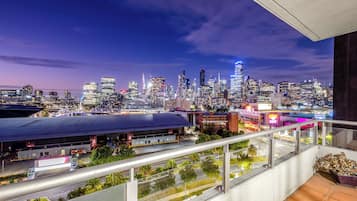 Une vue sur les gratte-ciel d’une ville au crépuscule, avec des bâtiments modernes, un parking et un balcon offrant une vue sur la ville.