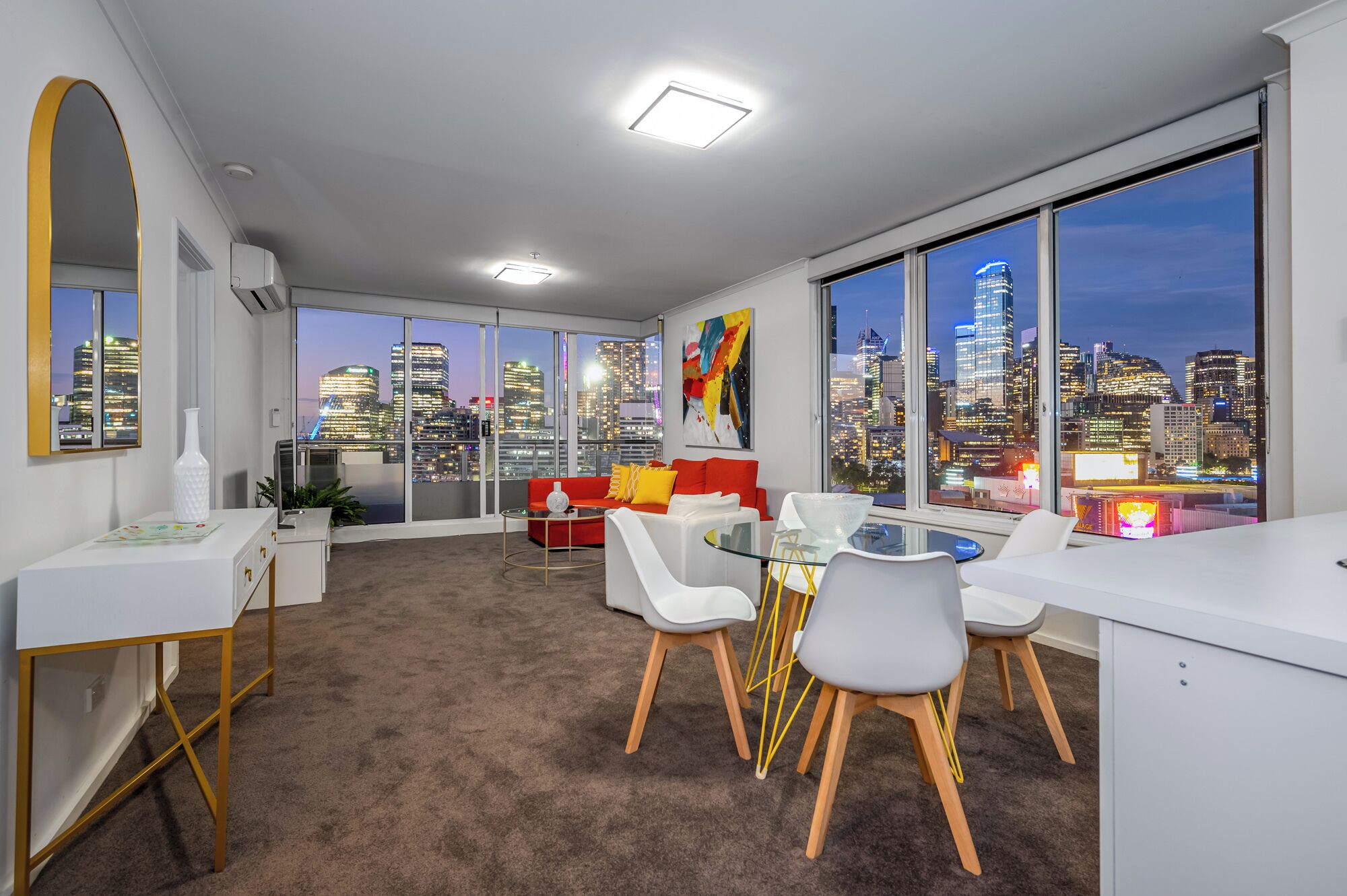 Un espace de bureau moderne avec vue sur la ville, comprenant une table ronde en verre, des chaises blanches et un canapé rouge.