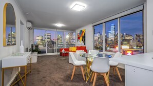 Een moderne kantoorruimte met uitzicht over de stad, met een ronde glazen tafel, witte stoelen en een rode bank.