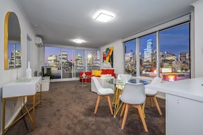 A modern office space with a city view, featuring a round glass table, white chairs, and a red sofa. - Exclusive Stays - Rivergarden (Southbank)