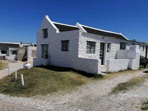 A white building with a sloped roof, a small porch, and a stone wall.