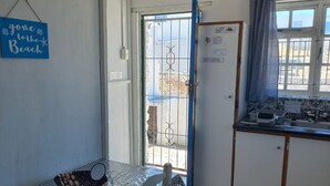 En lille tekøkken med vask, et vindue med gardin, en dør med skilt og et bord med ternet dug.