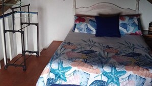 Et soveværelse med en seng, en hængende lampe, et skilt på væggen og et tøjstativ.