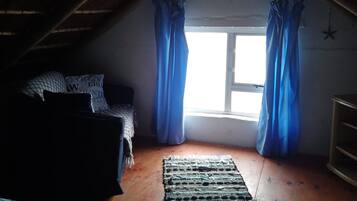 Une chambre mansardée avec un plafond en pente, un lit avec une literie à motifs, une fenêtre avec des rideaux bleus et un plancher en bois.