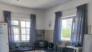 Et lille køkken med mikroovn, brødrister og køleskab. Der er et vindue med gardiner, et flisebeklædt bagpanel og et bord med ternet dug.
