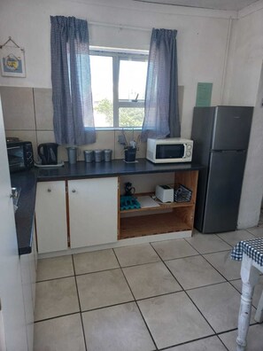 A compact kitchen with a microwave, toaster, kettle, and a refrigerator.