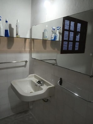 Un baño con un lavamanos blanco, un espejo y un estante con artículos de aseo.