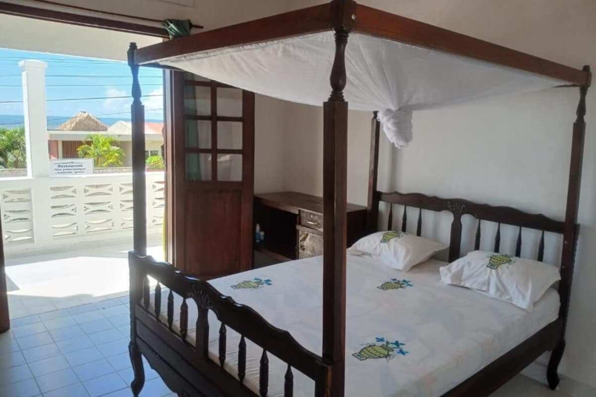 Una cama con dosel y cuatro postes, una mesita de noche de madera y vistas al océano.