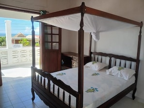 Una cama con dosel y cuatro postes, una mesita de noche de madera y vistas al océano.