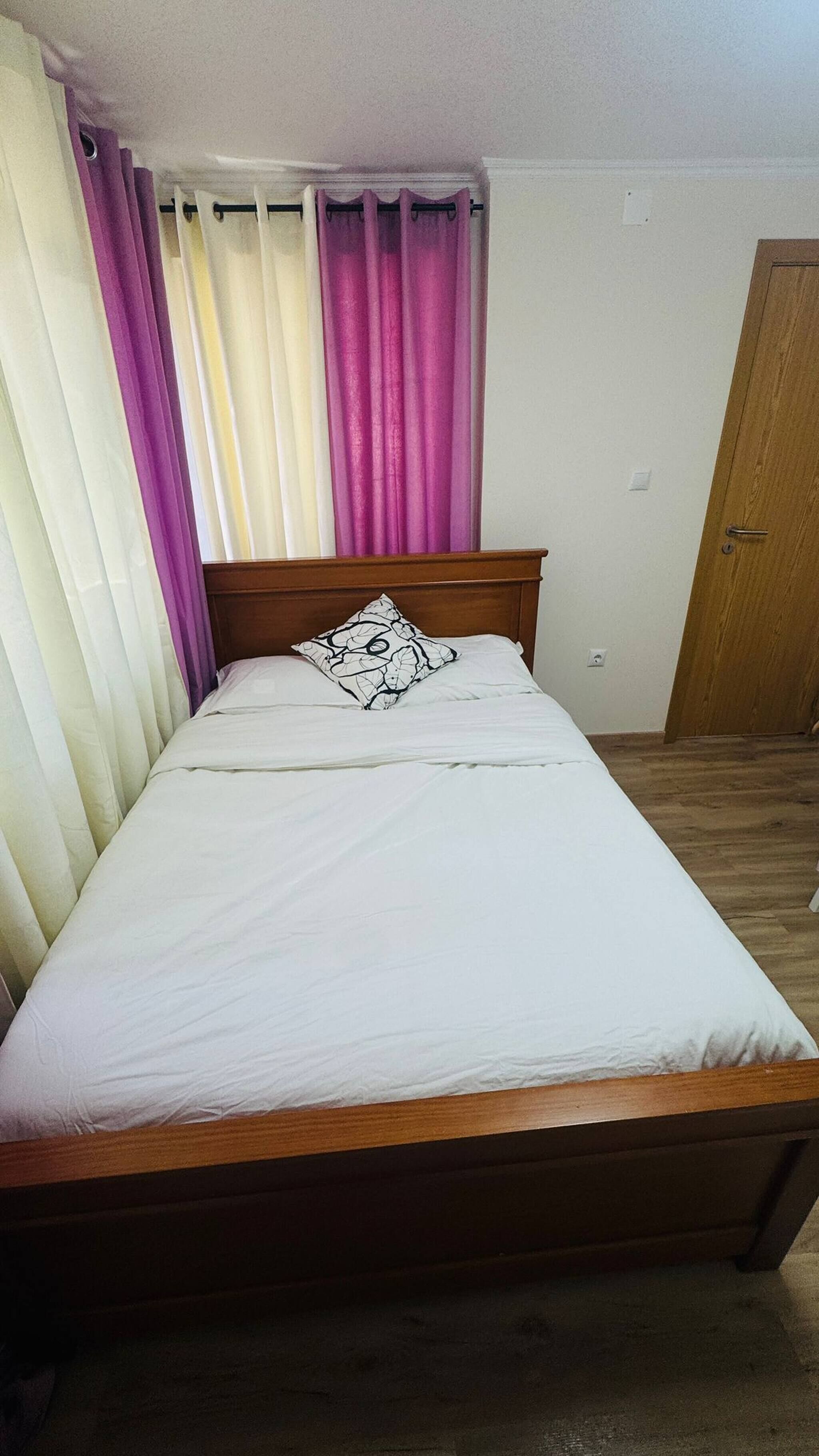 A single bed with a wooden headboard, white bedding, and a black and white pillow.
