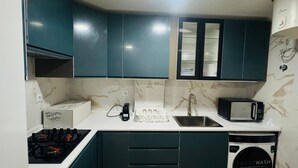 A compact kitchen with teal cabinets, a microwave, a sink, a stove, and a built-in washing machine. - Cozy 2-Bedroom Apartment in Pontinha, Portugal (Pontinha)
