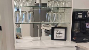 A bar area with a stool, a coffee machine, and a sign that says 'IN Coffee WE TRUST'.