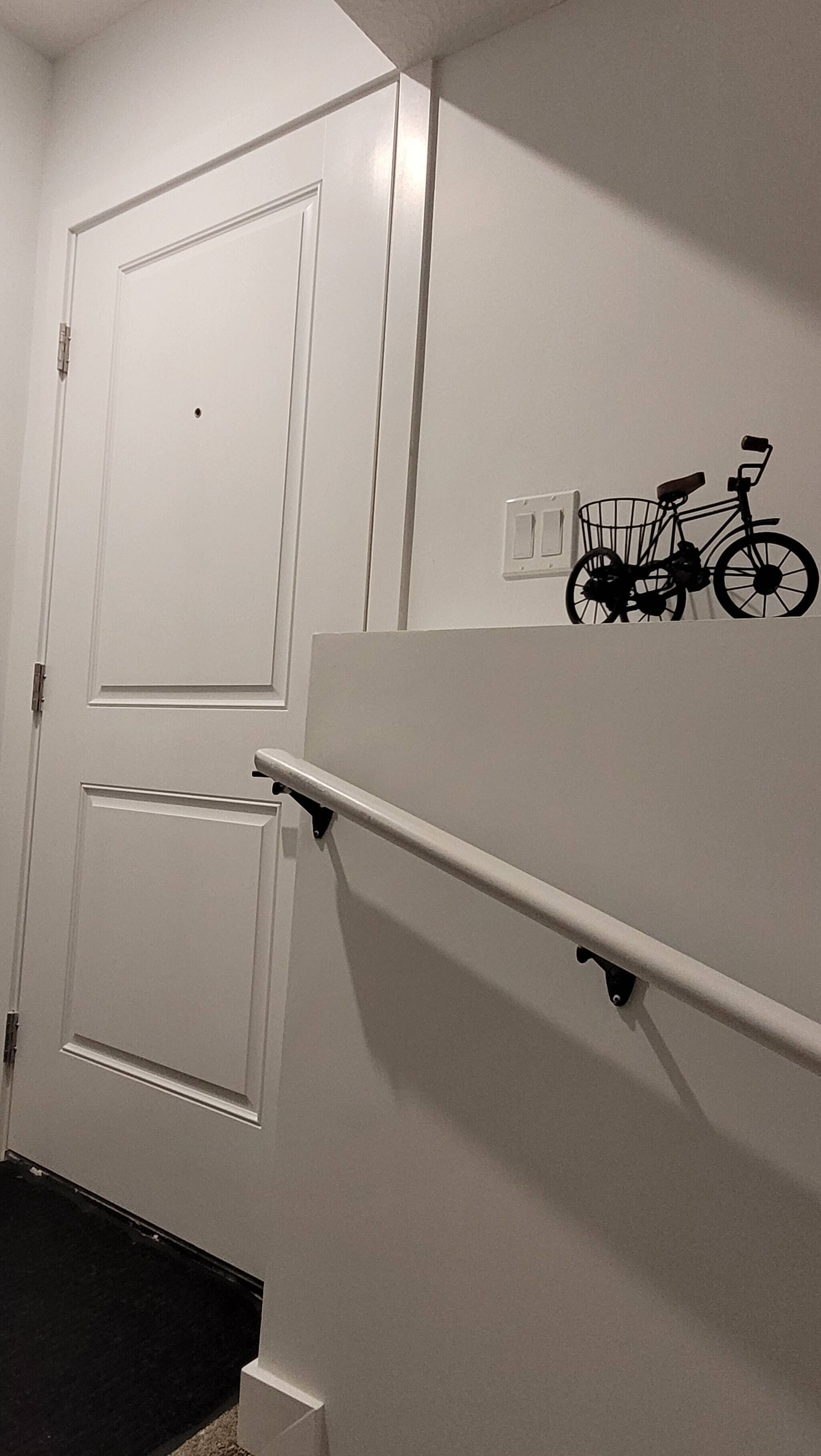 A white door with a small hole, a white wall with a light switch, and a bicycle silhouette decoration.