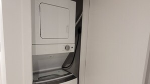 A compact laundry room with a built-in washer and dryer, a door with a handle, and a wooden floor.