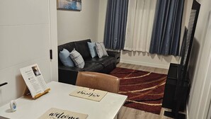 A compact living space with a dining table, a sofa, a piano, and a view of a building through the window.