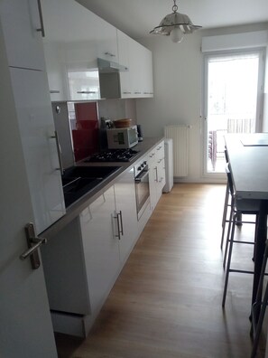 A modern kitchen with white cabinets, a red appliance, a microwave, and a stove. - FESTIVAL OF LIGHTS (Lyon)