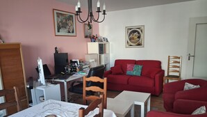 Ein Wohnzimmer mit einem roten Sofa, einem Esstisch mit Stühlen, einem Schreibtisch und einer Kandelaber.