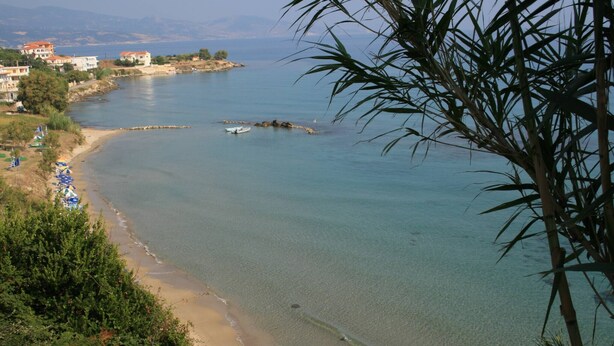 Una vista costiera con acqua limpida, una spiaggia sabbiosa e edifici sullo sfondo.