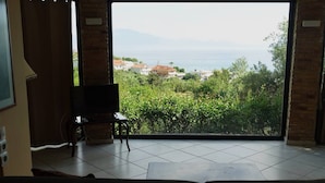 Una stanza con un'ampia porta-finestra scorrevole che si apre su un balcone con vista sul mare e sul verde.