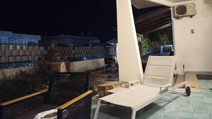 A balcony with a white chair, a small table, and a potted plant.