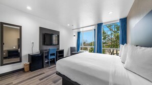 Una habitación de hotel con una cama grande, un escritorio con silla, un televisor montado en la pared y una ventana con cortinas.