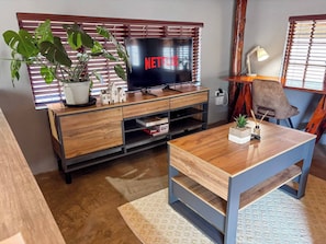 A living room with a TV, wooden entertainment unit, a potted plant, a lamp, and a chair.