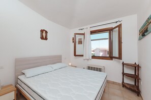 Ein Schlafzimmer mit einem Bett, einem Fenster mit Vorhängen, einem Heizkörper und einer Holzablage.