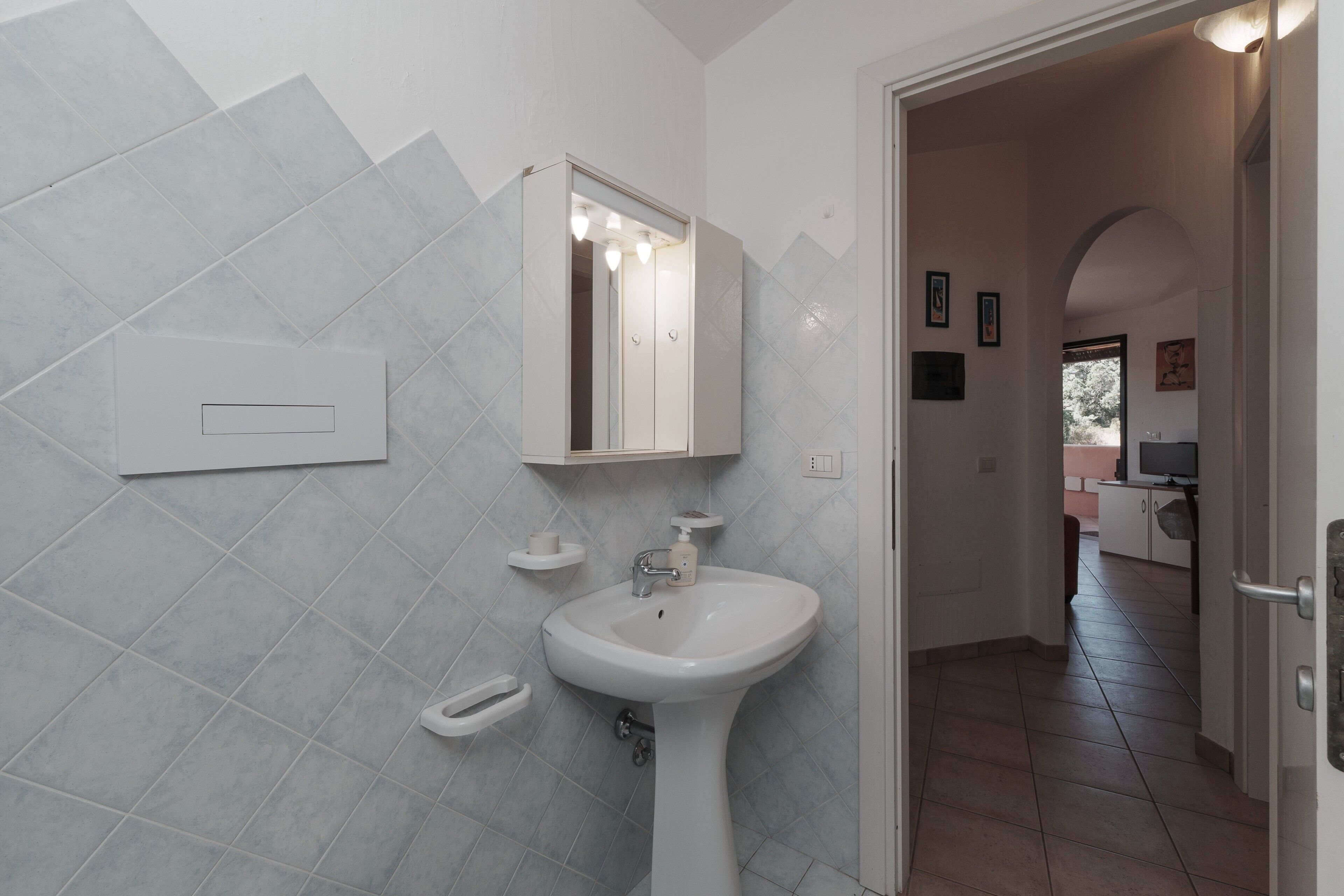 Ein Badezimmer mit einem Waschbecken auf Säule, einem Spiegel und einem Lichtschalter an der Wand.