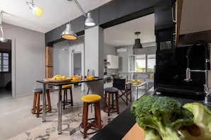 Une cuisine moderne avec un plan de travail noir, des tabourets en bois et un coin repas comprenant une table et des chaises.