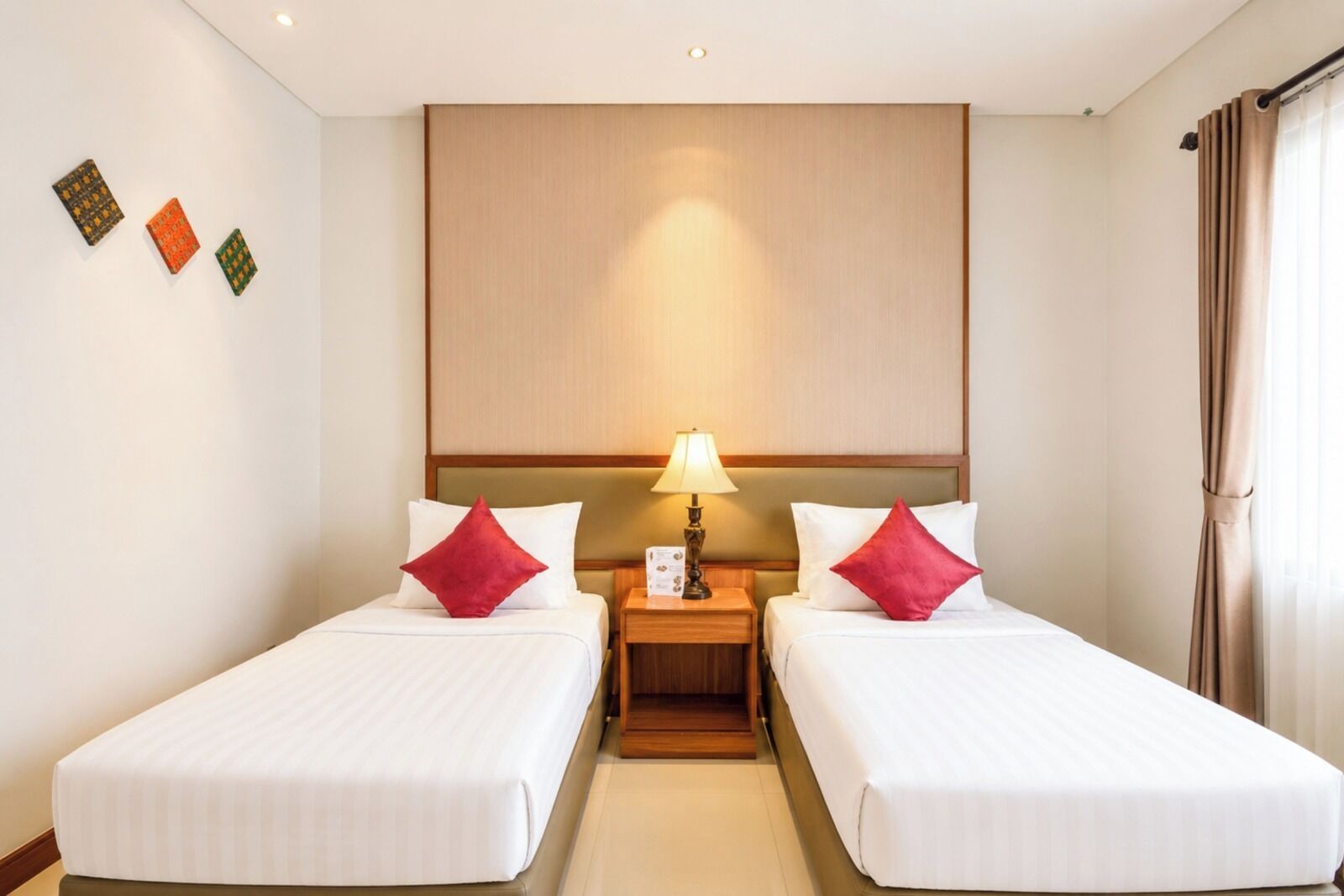 A hotel room with two beds, a nightstand with a lamp, and a wall-mounted panel above the beds.