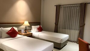 A hotel room with two single beds, a nightstand with a lamp, a chair, and a window with curtains. - Sany Rosa Hotel (Bandung)