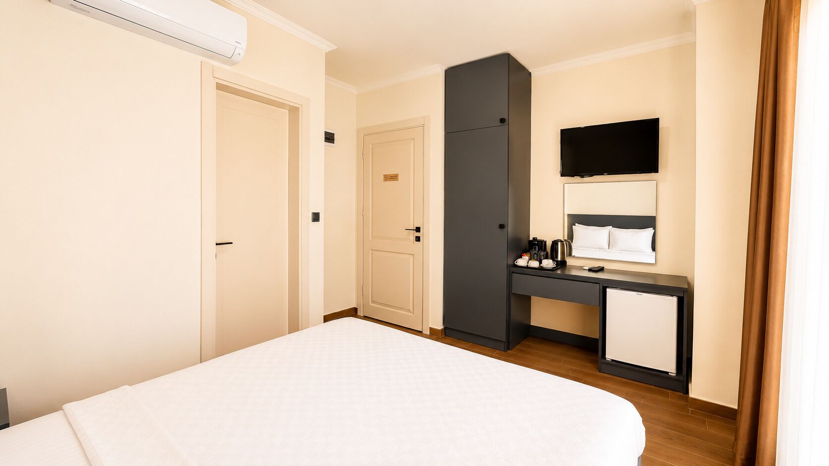 Una habitación de hotel con cama, escritorio con computadora, televisión y minibar.