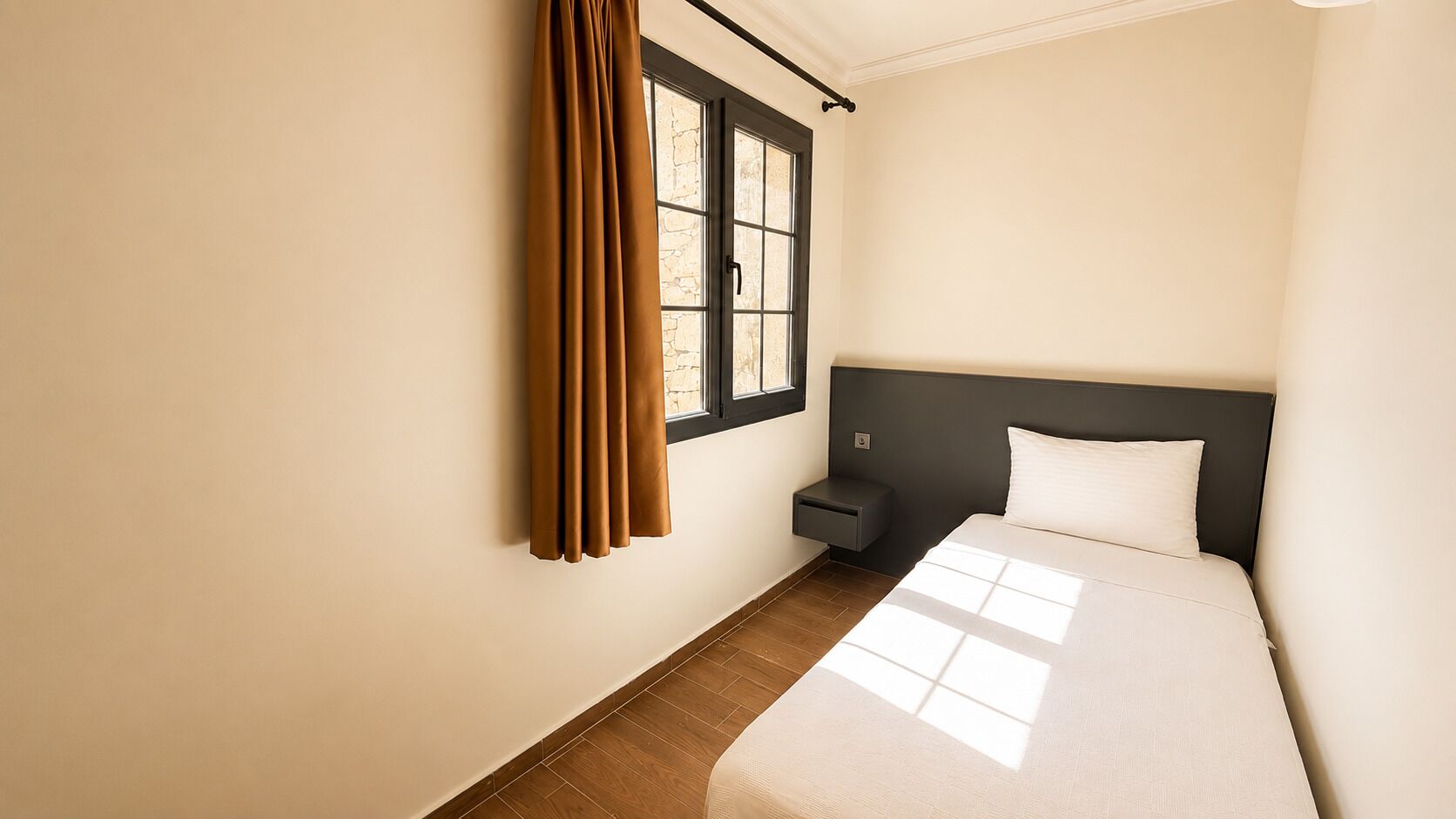 Un dormitorio con cama, mesita de noche, ventana con cortinas y vistas al exterior.