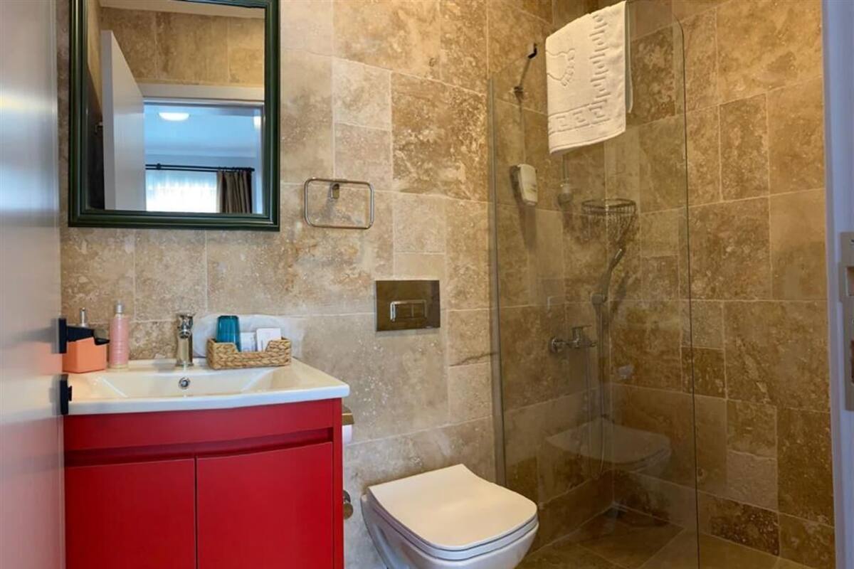 A bathroom with a glass shower enclosure, a red vanity, a white toilet, and a mirror with a green frame.