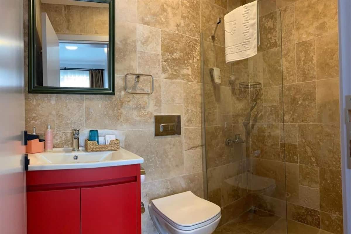 Une salle de bain avec une douche à parois de verre, un meuble-lavabo rouge, des toilettes blanches et un miroir avec un cadre vert.