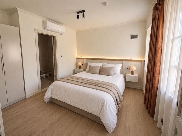 Habitació d'hotel amb llit, taules de nit, un aparell d'aire condicionat i una porta al bany.