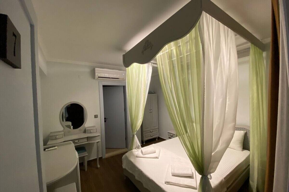 A bedroom with a four-poster bed, a bedside table, a mirror, and a wardrobe.