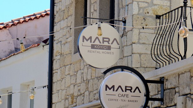 A building with multiple signs for 'MARA KÖYÇİ RENTAL HOMES' and 'MARA CAFE,' indicating a commercial area with rental properties and a cafe.