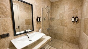 A bathroom with a white sink, a large mirror, a shower with a glass door, and two bottles of shampoo on the wall.