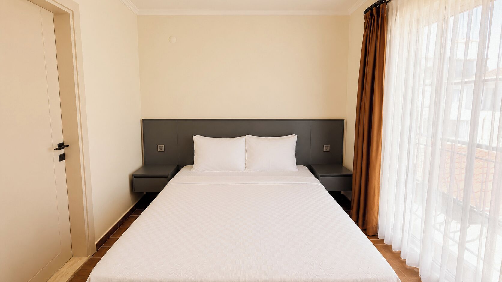 Una camera d'albergo con un letto, comodini, una porta e tende leggere.