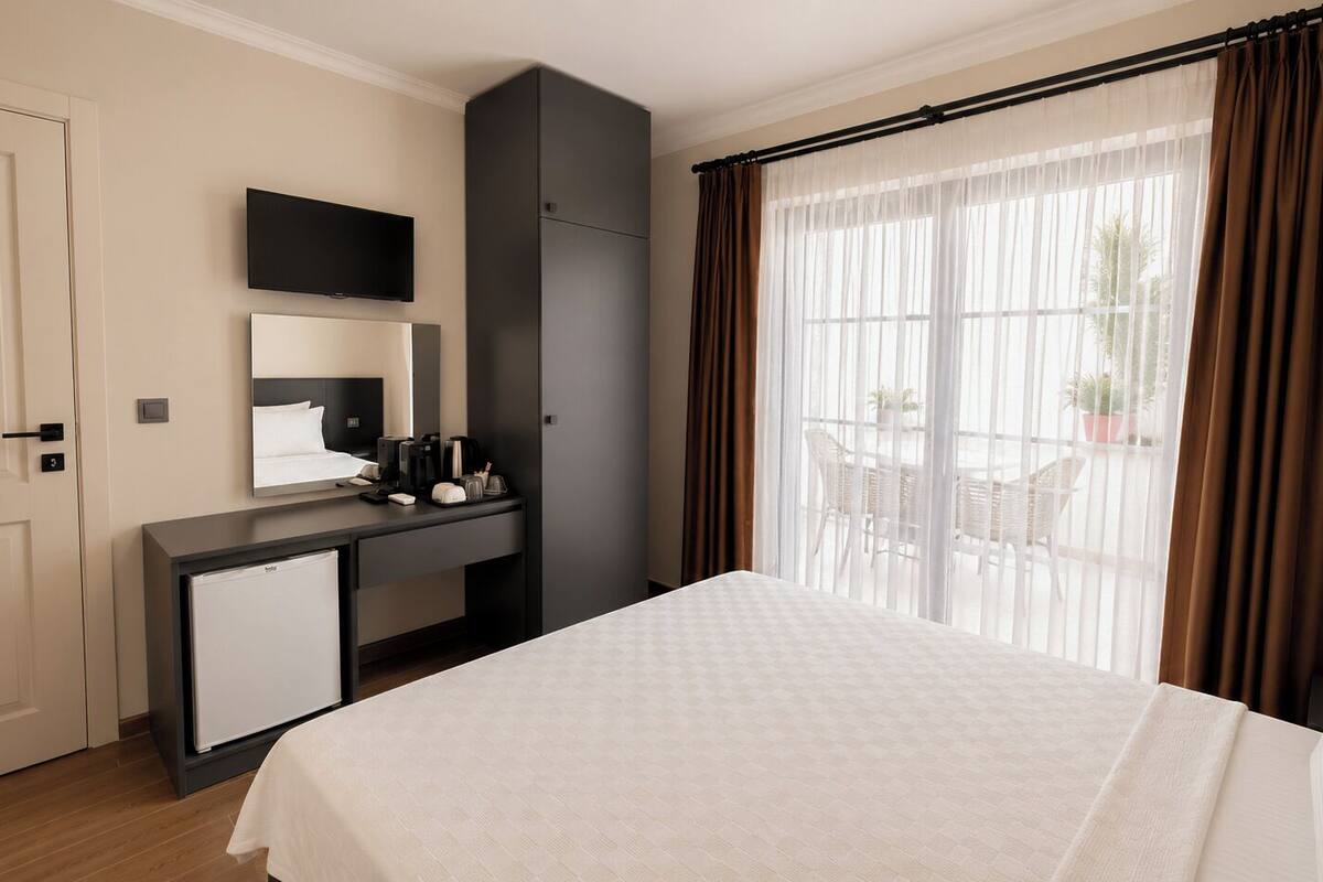A hotel room with a bed, a desk with a computer, a television, and a window with curtains.