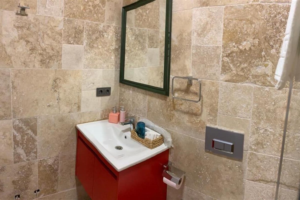A bathroom with a red vanity, a mirror, a sink, and a shower area.