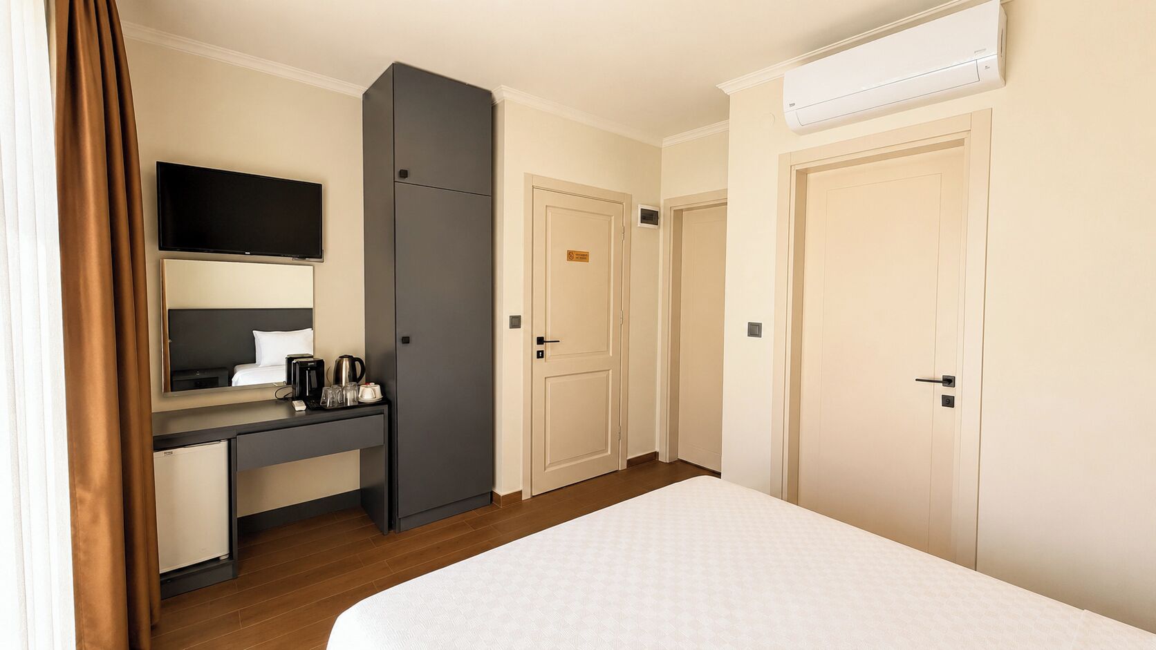 Une chambre d’hôtel équipée d’un lit, d’un bureau avec un téléviseur à écran plat, d’un mini-réfrigérateur, d’une machine à café et de deux portes.